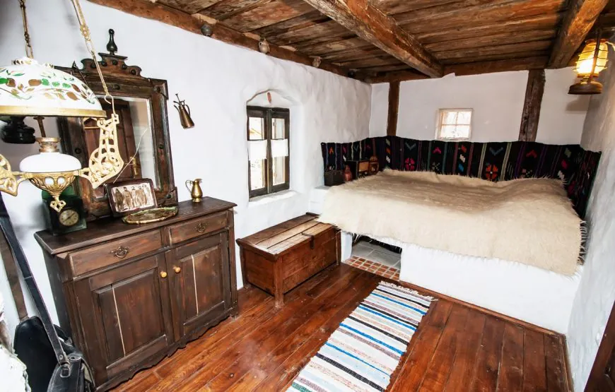 Cameră în Casa de Lut, cu pat cu cergă, lampă veche și mobilier de lemn