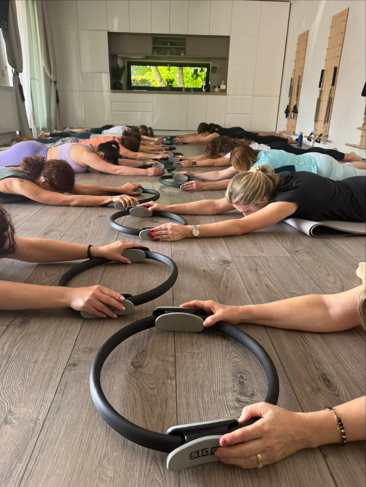 Clasă de grup: cursante întinse pe burtă, cu cercuri de pilates în mâini