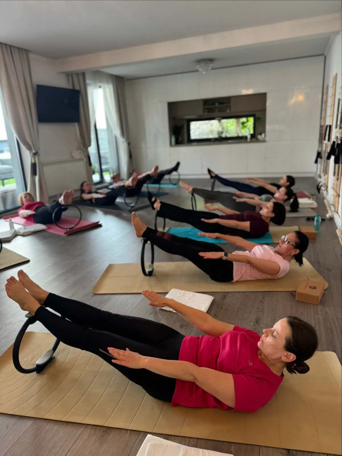 Oră de grup pe saltele, cu cercul de pilates prins între glezne