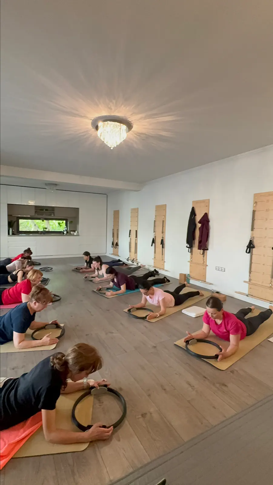 Sala Pilates Studio No8: podea de lemn, spaliere pe perete și o grupă la lucru